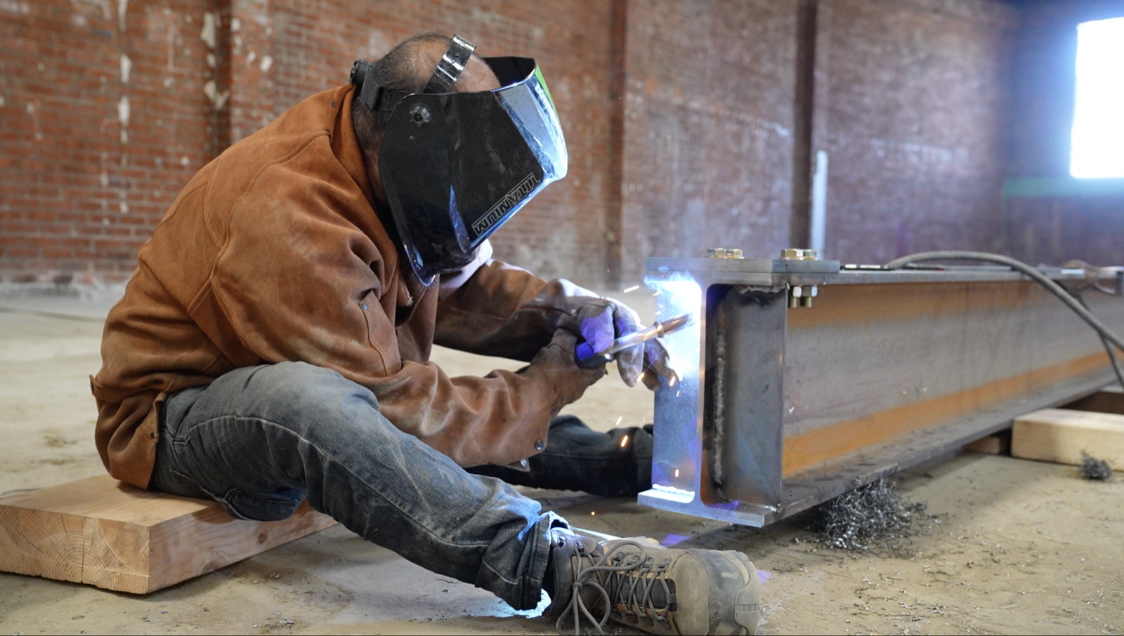 Welder fabricating a steel beam connection for a construction project